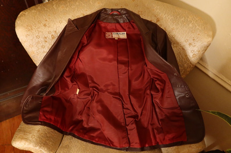 May include: A brown leather jacket with a red satin lining. The jacket has a button closure and a label that reads "GIBRALAN".