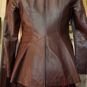 May include: A brown leather jacket with a fitted silhouette and a single-breasted closure. The jacket has a smooth, polished finish and features a classic design.
