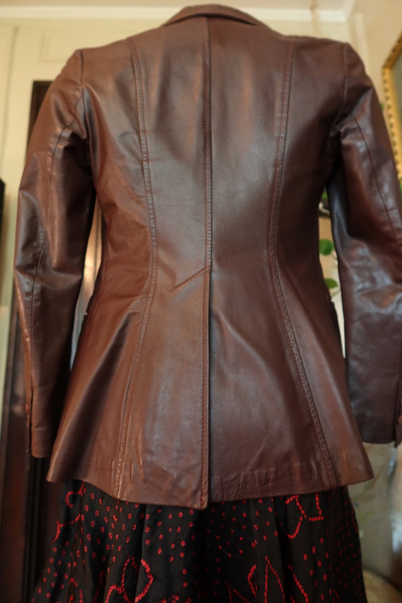 May include: A brown leather jacket with a fitted silhouette and a single-breasted closure. The jacket has a smooth, polished finish and features a classic design.