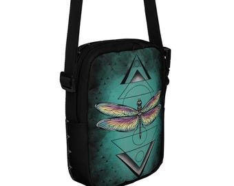 May include: Black crossbody bag with a teal background featuring a colorful dragonfly design and geometric shapes. The bag has a black adjustable strap and a small side pocket. The dragonfly has rainbow-colored wings.