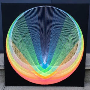 Könnte beinhalten: Ein lebendiges String-Art-Stück mit einem kreisförmigen Regenbogen-Design auf schwarzem Hintergrund. Das Kunstwerk verwendet Fäden in Pink, Orange, Gelb, Grün und Blau, wodurch eine visuell auffällige und moderne Ästhetik entsteht. Einzigartige Wanddekoration.