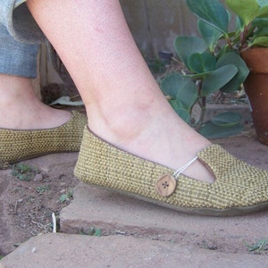 May include: A pair of woven, beige flats with a button detail on the strap. The shoes have a closed toe and a low heel.