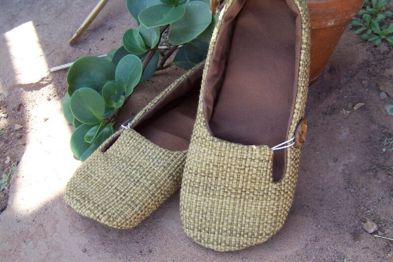 May include: A pair of brown woven flat shoes with a brown fabric lining. The shoes have a simple design and are made of a natural material.