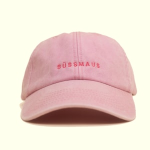 Könnte beinhalten: Hellrosa Baseballkappe mit dem Wort "SÜSSMAUS" in passendem rosa Garn gestickt. Die Kappe hat einen gebogenen Schirm und eine strukturierte Krone.