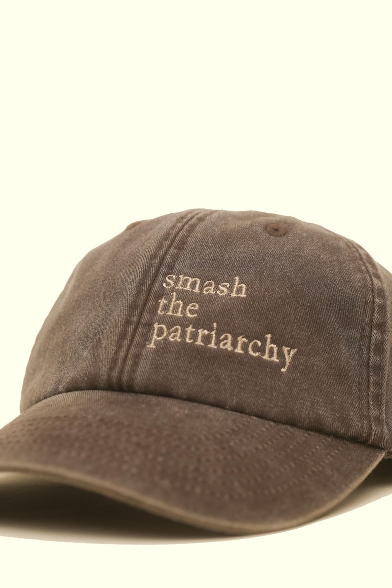 Op de afbeelding: Bruine baseballcap met de geborduurde tekst "smash the patriarchy" in lichtbruin. De cap heeft een gebogen klep en een klassiek zes-panelen ontwerp, geschikt voor dagelijks gebruik.