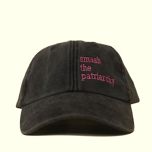 Op de afbeelding: Zwarte baseballcap met de roze geborduurde tekst "smash the patriarchy". De cap heeft een gebogen klep en een verstelbare band, een casual accessoire voor dagelijks gebruik.