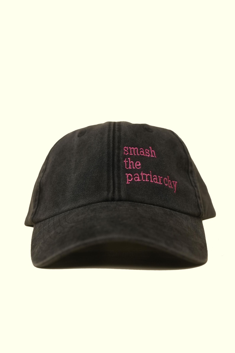 Op de afbeelding: Zwarte baseballcap met de roze geborduurde tekst "smash the patriarchy". De cap heeft een gebogen klep en een verstelbare band, een casual accessoire voor dagelijks gebruik.
