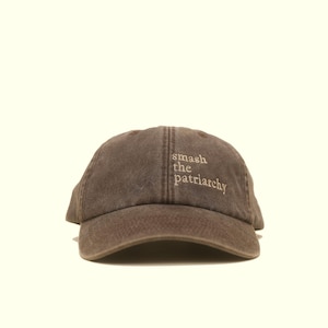Op de afbeelding: Bruine baseballcap met de geborduurde tekst "smash the patriarchy" in een lichtere bruine kleur. De cap heeft een gebogen klep en een klassiek zes-panelen ontwerp.