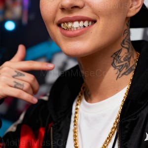 May include: Close-up of a person smiling, showing gold teeth grillz. The person is wearing a gold chain necklace and a black jacket. The image also shows a tattoo on the neck and a hand with a tattoo.