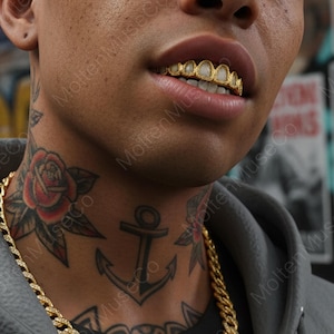 May include: Close-up of a person's mouth with gold teeth. The teeth are detailed with a decorative design. The person has a gold chain necklace and tattoos on their neck, including a rose and an anchor.