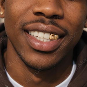 May include: A gold tooth grill covering two teeth, featuring an engraved cross design on one piece and a four-pointed star emblem on the other. The metallic gold accessory is fitted over the upper teeth, showcasing detailed craftsmanship and texture.