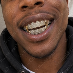 Könnte beinhalten: Ein Set aus goldenen Grillz für die oberen und unteren Zähne, das mit einem dichten Pavé-Besatz aus kleinen, klaren, reflektierenden Steinen auf den Vorderseiten versehen ist, mit glatten, polierten Goldkappen auf den äußeren Zähnen.