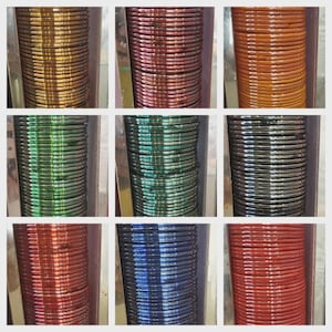 Puede incluir: Nueve pilas de pulseras coloridas en una cuadrícula cuadrada. Las pulseras son de varios colores, incluyendo oro, rojo, naranja, verde, azul y plata. Cada pila está contenida dentro de una caja de color plateado, creando una exhibición visualmente atractiva.