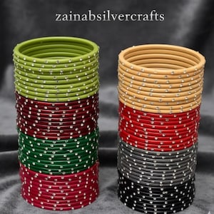 May include: A collection of colourful bangles in shades of green, red, and tan, each decorated with small, sparkling embellishments. The text "zainabsilvercrafts" is visible at the top. These bangles are a vibrant accessory.