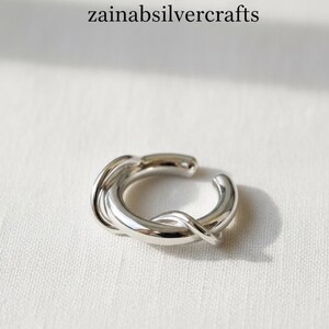 May include: A silver ear cuff with a twisted design. The ear cuff is made of shiny metal and has a smooth, polished surface. The text "zainabsilvercrafts" is at the top of the image.