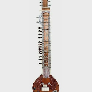 May include: A sitar, a long-necked stringed instrument, is displayed against a white background. The instrument features a wooden neck and body, with intricate carvings and metal detailing. The sitar has multiple strings and tuning pegs.