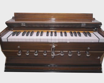 Pode incluir: Um harmónio de madeira com teclado e vários botões prateados. O instrumento tem um acabamento castanho escuro brilhante e uma forma retangular. As teclas são brancas e pretas.