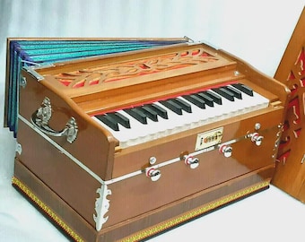 Pode incluir: Um harmônio marrom com teclado, detalhes prateados e um topo decorativo. O instrumento tem um interior vermelho e um fole colorido em estilo acordeão. O teclado possui teclas pretas e brancas.