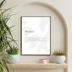 May include: A framed print with the word "Shibui" in a minimalist design. The definition of Shibui is included below the word. The print is displayed on a wooden shelf with decorative plants and books.