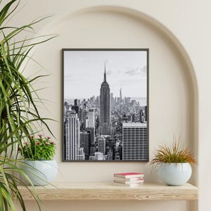 Könnte beinhalten: Schwarz-Weiß-Druck mit Rahmen der Skyline von New York City, mit dem Empire State Building im Mittelpunkt. Das Bild zeigt die Wolkenkratzer und die urbane Landschaft der Stadt.