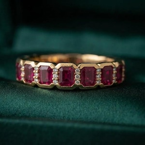 May include: A gold band ring featuring a series of alternating emerald-cut red rubies and small round white diamonds. The stones are set in a continuous row around the circumference of the metal band, creating a repeating pattern of gemstones.