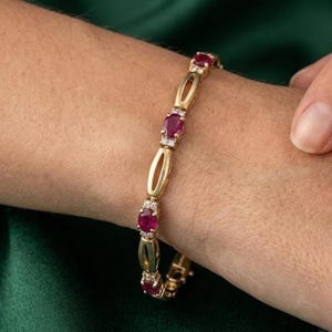 May include: Gold bracelet featuring oval-cut red gemstones and small clear accent stones. The bracelet has a delicate design with open oval links. The gemstones are set in a gold band, creating a classic and elegant look.