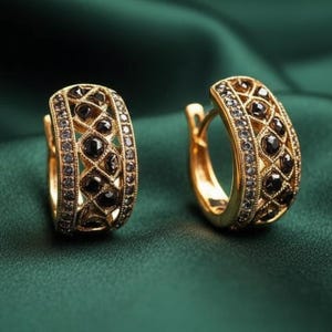 May include: A pair of gold-toned hoop earrings with intricate openwork and black gemstone accents. The earrings feature a geometric design with a row of small black stones along the edges and larger black stones in the center. The earrings are displayed on a dark green background.