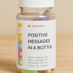May include: A clear glass bottle with a white lid, labeled "POSITIVE MESSAGES IN A BOTTLE" with instructions. The bottle contains colorful capsules. The brand name "SENSEMORY" is visible.