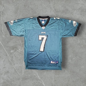 Könnte beinhalten: Ein tealfarbenes Philadelphia Eagles Football-Trikot mit schwarzem Besatz, das auf der Vorderseite die Nummer 7 in Weiß mit schwarzer Umrandung, das Wort Eagles über der Nummer und Reebok-Logos auf beiden Ärmeln sowie ein NFL-Logo zeigt.
