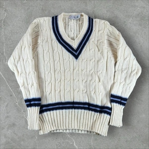 May include: A cream-colored cable knit sweater featuring a V-neckline with navy blue and light blue striped trim. The long-sleeved garment includes matching navy and light blue horizontal stripes at the ribbed cuffs and the bottom hemline.