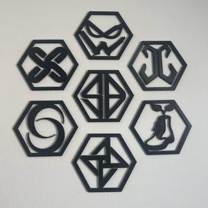 May include: Seven black geometric wall decorations in a honeycomb shape. Each hexagon contains a unique design, including abstract shapes, symbols, and a stylized boot with a plant. The decorations are mounted on a white wall.