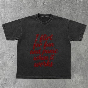 May include: Dark gray t-shirt with the text "I flirt for fun and panic when it works" in red script. The shirt has a vintage, washed appearance and a crew neck.