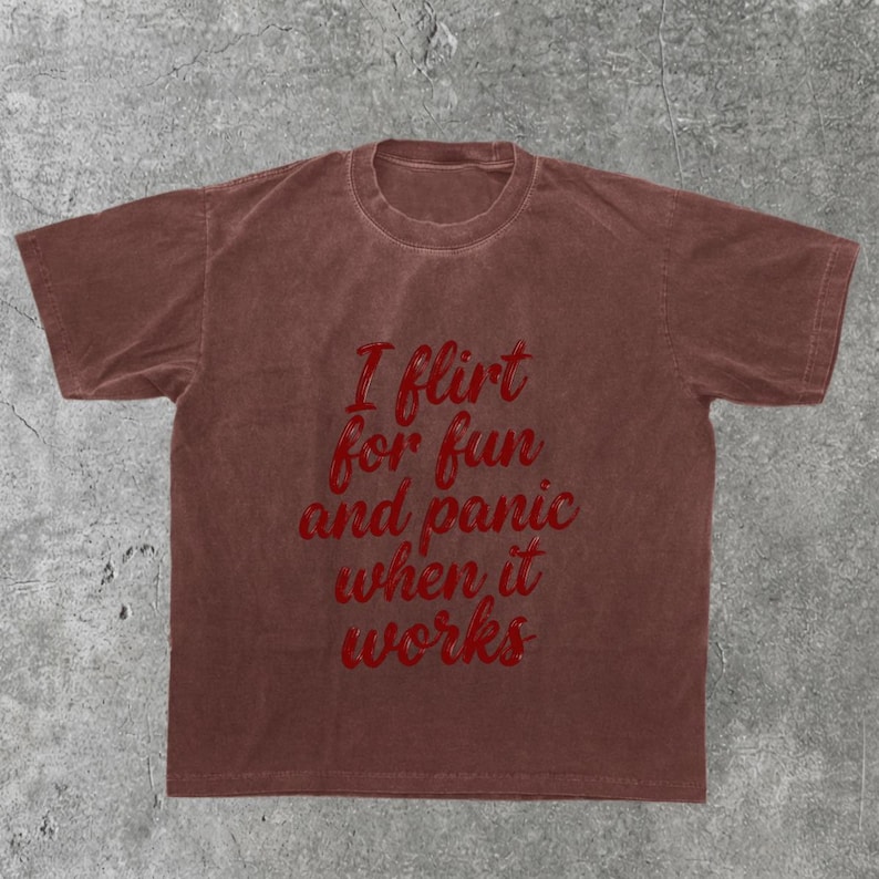 May include: A brown t-shirt with the text "I flirt for fun and panic when it works" in red script. The shirt is a solid color and has a crew neck.