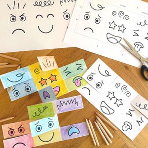 Pode incluir: Um conjunto de cartões de emoções e folhas de trabalho desenhadas à mão. Os cartões apresentam várias expressões faciais, incluindo feliz, triste e zangado. Lápis e tesouras também estão presentes, sugerindo uma atividade artesanal ou educativa.