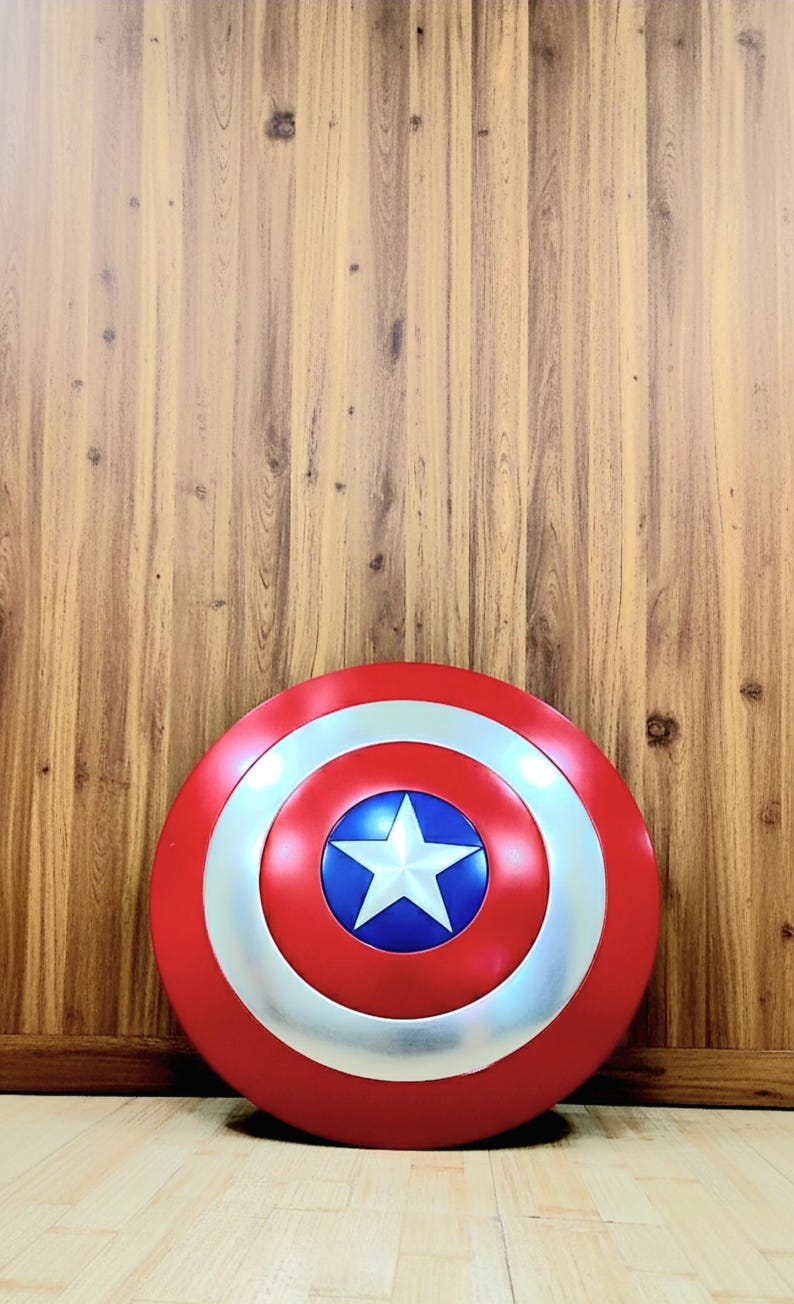 May include: A red, white, and blue shield with a star in the center. The shield is round with a silver ring around the center star. The background is a wooden wall and floor.