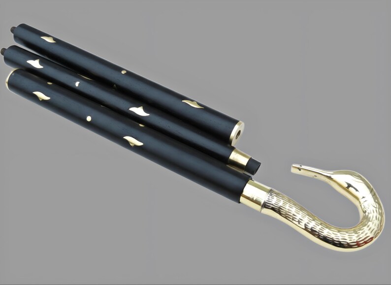 May include: A black folding cane with gold accents. The cane features a swan-shaped handle and decorative gold leaf-shaped cutouts. The handle and the ends of the cane are gold. The cane is folded and angled across a gray background.