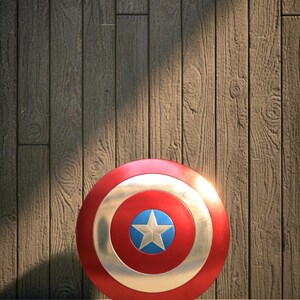 May include: A red, white, and blue Captain America shield with a star emblem. The shield is round and metallic, resting on a stone surface against a wooden background. The shield is a popular item for cosplay and superhero fans.