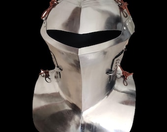 Puede incluir: Un casco medieval pulido de color plateado, con visera puntiaguda y protector de cuello. El casco tiene remaches y correas de cuero para la fijación. El diseño es reflectante, con fondo oscuro.