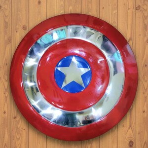 May include: A red and silver shield with a blue and white star in the center. The shield has a circular design with a red outer ring, a silver middle ring, and a red center with a blue circle and white star.