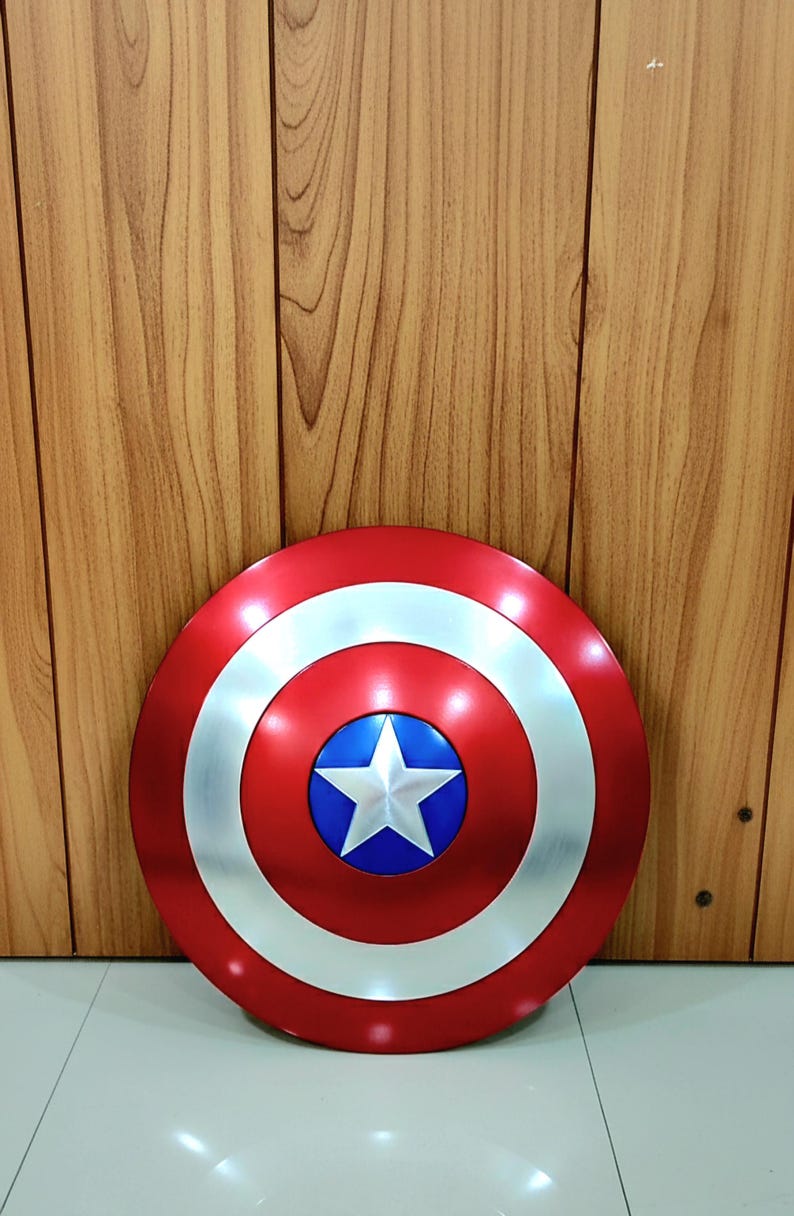 May include: A red, white, and blue Captain America shield. The shield is round with a silver outer ring, a red center, and a blue circle with a white star in the middle. The shield is a prop or collectible.