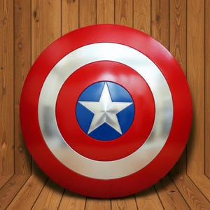 May include: A red, white, and blue shield with a silver star in the center. The shield has a circular design with a silver ring and a blue center. The shield is a prop or collectible.