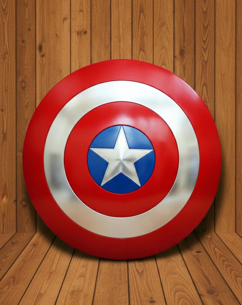 May include: A red, white, and blue shield with a silver star in the center. The shield has a circular design with a silver ring and a blue center. The shield is a prop or collectible.
