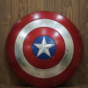 May include: A round shield with a red outer ring, a silver inner ring, and a blue center with a silver star. The shield is displayed against a wooden background.