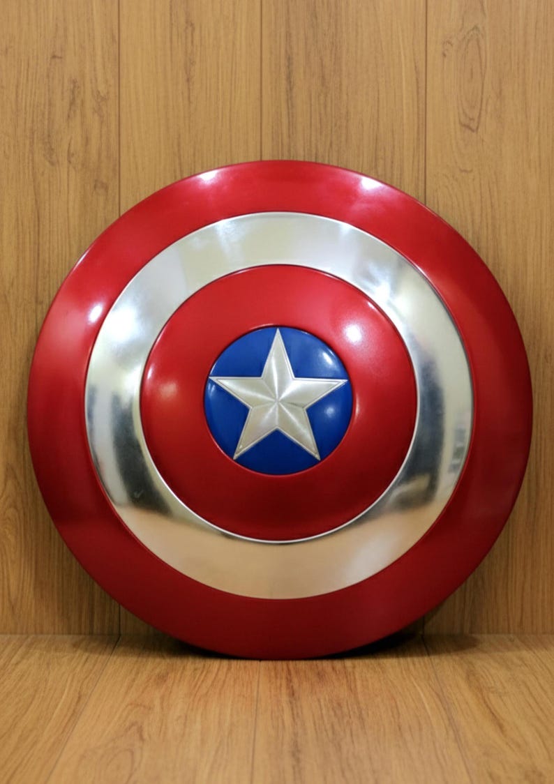 May include: A red, white, and blue shield with a star in the center. The shield has a circular design with a silver border and a blue circle in the middle, featuring a white star.