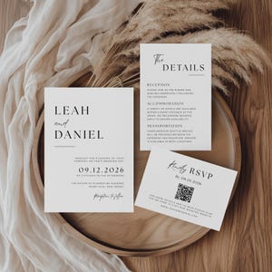 May include: A stylish wedding invitation suite comprising three cards with a minimalist design. The main card displays the names "LEAH and DANIEL" and wedding details. Additional cards provide RSVP and event information. The suite is set on a wooden tray.