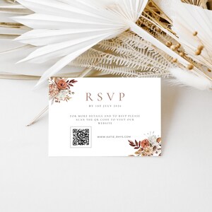 May include: A white RSVP card with floral accents in shades of brown and cream. The card includes the text "RSVP by 1st July 2026", a QR code, and website information. The card is decorated with dried flowers.