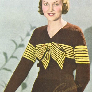 May include: A woman wearing a brown sweater with yellow stripes and a bow. The sweater has a V-neck and is knitted. The woman is standing in front of a light blue background.