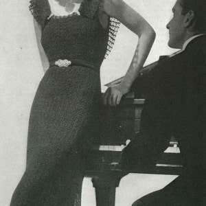 May include: A woman in a black crochet dress with a flower in her hair stands next to a man in a suit. The woman is holding onto the piano.