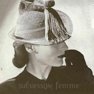 Puede incluir: Una foto en blanco y negro de una mujer con un sombrero de ganchillo con un borla. El sombrero es de color gris claro y tiene un ala ancha. La mujer lleva una blusa de color oscuro y tiene el pelo recogido hacia atrás.