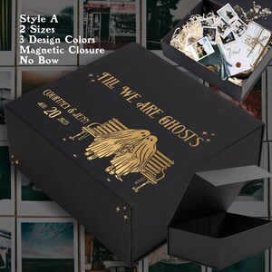 May include: A black gift box with gold lettering and design. The box reads "Till We Are Ghosts" and features two ghost figures on a bench. The box also includes the names "Courtney & Jenn" and the date "Aug 20 2025".